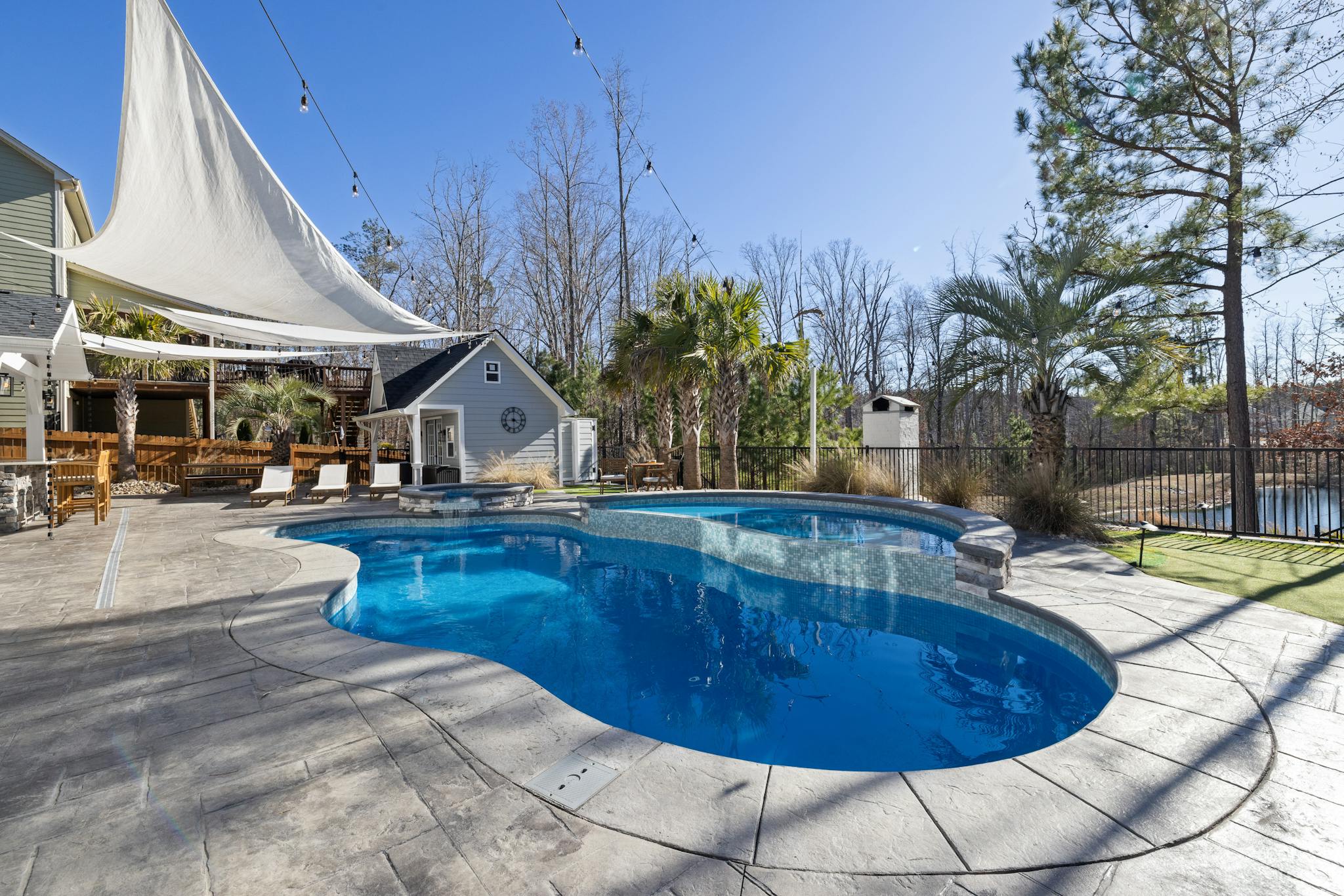 A sunny backyard oasis featuring a luxurious pool, deck, and palm trees, perfect for relaxation.